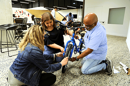 Three corporate participants collaborating on the professional assembly of a bicycle during a LEVEL 12 team building session.